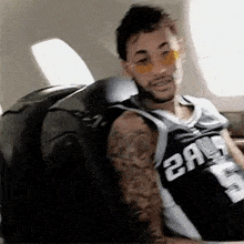 a man wearing sunglasses and a jersey is sitting on a plane .