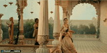 a woman in a white dress is standing in a room with columns and the words pranay varma on the bottom right