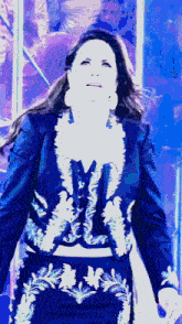 a woman in a blue jacket and white embroidery is standing in front of a blue background