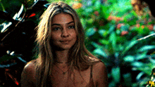a woman with long blonde hair is standing in front of a bush .