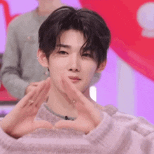 a young man in a striped sweater is making a heart with his hands .
