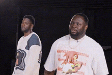 two men are standing next to each other and one of them is wearing a knuckles shirt .