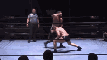 a referee watches two men wrestle in a ring with the word glory on the wall behind them