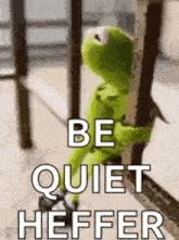 kermit the frog is sitting on a railing with the words `` be quiet heffer '' written on it .
