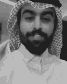 a black and white photo of a man with a beard wearing a keffiyeh and smiling .