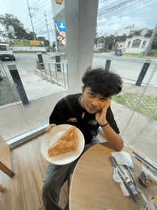 a young man is sitting at a table holding a plate of food with a slice of pie