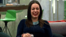 a woman is sitting on a couch laughing while holding a glass of wine .
