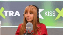 a woman wearing headphones is talking into a microphone in front of a sign that says kiss .