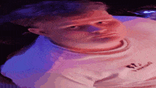a man in a white shirt is sitting in a dark room with purple lights behind him .
