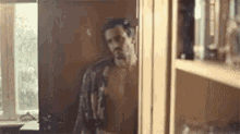 a shirtless man is standing in a kitchen next to a window .