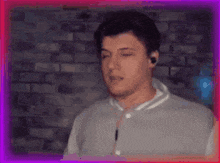 a man wearing ear buds is standing in front of a brick wall with his eyes closed .