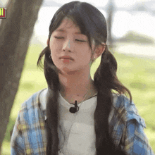 the girl is wearing pigtails and a plaid shirt and has a microphone around her neck .
