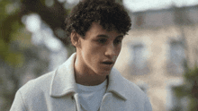 a young man with curly hair is wearing a white jacket and a white t-shirt