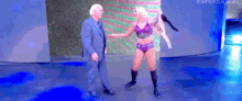 a man in a suit is standing next to a woman in a purple bikini .