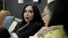 two women are sitting on a couch with their mouths open and one of them is holding a cell phone .