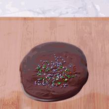 a chocolate cookie with sprinkles on it on a wooden surface