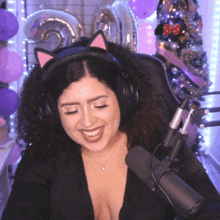 a woman wearing headphones and a cat ear headband is smiling in front of a microphone