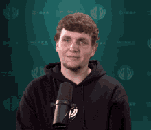 a man in a black hoodie stands in front of a microphone with a green background that says hirez