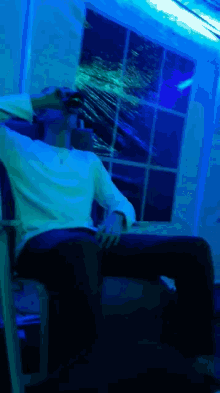 a man in a white shirt is sitting in a dark room with blue lights behind him