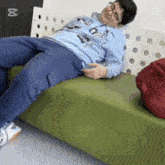 a man in a blue shirt is laying on a green couch