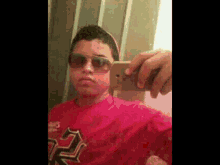 a young boy wearing sunglasses is taking a selfie with a cell phone .