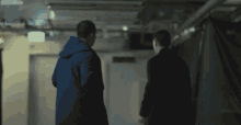 two men are walking down a hallway with a fire exit sign on the wall