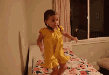 a little girl is jumping on a bed wearing a yellow dress .