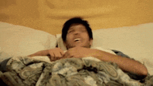 a man is laying on a bed with a blanket and laughing .