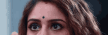 a close up of a woman 's face with a small black dot on her forehead .