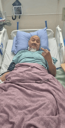 a man laying in a hospital bed with a purple blanket