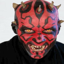 a man with red face paint and horns on his head is smiling