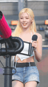 a woman in a white crop top and blue shorts is holding a microphone