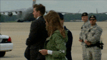 a man in a suit and a woman in a green jacket are standing on a runway