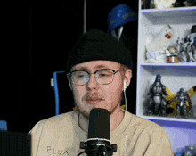 a man wearing glasses and a beanie is speaking into a microphone with elon written on his shirt