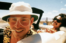 a man wearing sunglasses and a hat smiles while sitting in a car