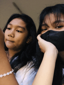 a girl wearing a black mask and a girl wearing a bracelet with the letter o on it