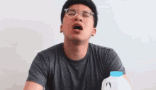 a man wearing glasses is yawning next to a milk jug .