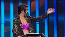 a woman in a leopard print jacket stands in front of a podium and says perfecto
