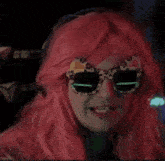 a woman wearing a pink wig and leopard print sunglasses looks at the camera