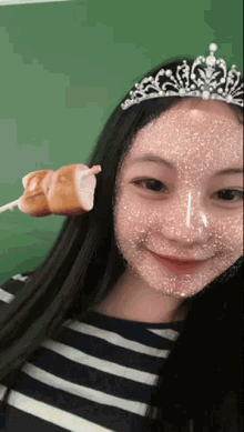 a girl wearing a tiara is holding a stick with a sausage on it .