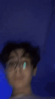 a young man wearing glasses and a white shirt is standing in a dark room .