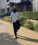 a man wearing a white t-shirt and black pants is walking down a sidewalk .