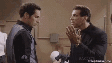 two men are standing next to each other in a room and talking .