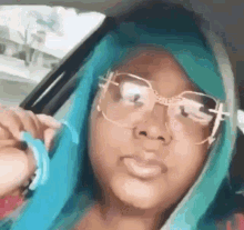 a girl with blue hair and glasses is sitting in a car and taking a selfie .