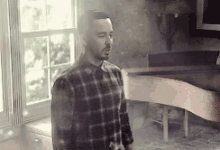 a man in a plaid shirt is standing next to a piano in a room .