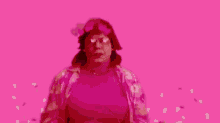 a woman wearing glasses and a pink headband with hearts on it is making a peace sign in a dark room .