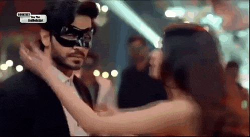 a man wearing a mask is being kissed by a woman in a red dress .