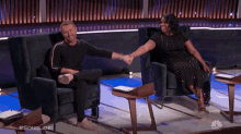 a man and woman are shaking hands while sitting in chairs on a stage .