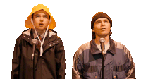 a man wearing a yellow hat is singing into a microphone next to another man