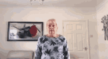 an elderly woman is standing in a living room with a picture of a rose on the wall .